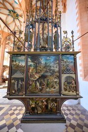<p>Die Rückseite des Bergaltars schmückt ein einmaliges Bergbaugemälde von Hans Hesse, der damals in Buchholz lebte und auf dem Bild 1521 das bergmännische Gewimmel vor seiner Tür einfing: die Abläufe über Tage rund um Halden, Schächte, Erzwäschen bis hin zur Münzpräge, die Arbeit der Haspelknechte und Erzausschläger, aber auch die Frau des Bergmanns setzte er ins rechte Licht.</p>
