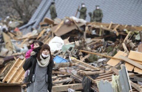 <p>
	Eine Mutter trägt ihr Kind durch die zerstörten Straßen von Ofunato.</p>
