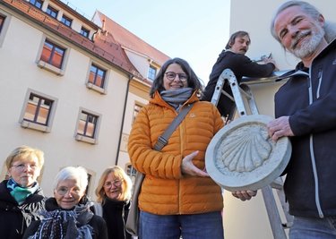Steinmetz- und Steinbildhauermeister Tobias Neubert (r.) und Initiatorin Sabine Lohmann mit der neuen Jakobsweg-Markierung an der Mönchstraße in Freiberg. Gemeinsam mit ihnen freuen sich drei der zehn Sponsorinnen und Geselle Sebastian Klar. 