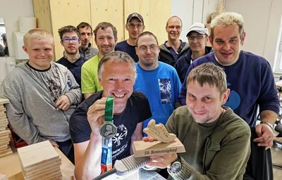 Dirk Lupke (vorn links) wurde nach dem Rennsteiglauf von seinen Kollegen mit einer selbst gefertigten Trophäe überrascht. Marcel Schuhmann (rechts) hat das Teil mit der Laubsäge ausgesägt. 