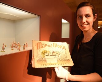 Museumsleiterin Tina Reitz zeigt ein historisches Sammelbilder-Album zu Max und Moritz. Es ist in der Sonderausstellung über Wilhelm Busch zu sehen. 
