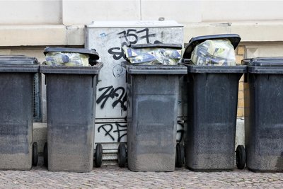 Volle Mülltonnen für Restmüll stehen an einer Hauswand (Symbolbild). Ab Januar 2024 sollen die Müllgebühren in Mittelsachsen steigen.