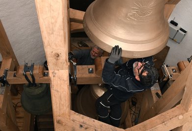 Torsten Kretschmer und Stefan Lein von den Herforder Elektromotorenwerken befestigen die neuen Bronzeglocken am neu gefertigten hölzernen Glockenstuhl. Mitarbeiter der Firma hatten bereits im April das alte Geläut im Kirchturm abgenommen. 