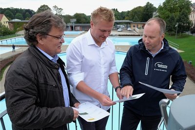 Baufachbereichsleiter Sven Hörning, Chris Kummer, Junior-Chef von Elektro-Kummer, und Stadtwerke-Geschäftsführer Lars Lange (v. l.) im Freibad Reichenbach beim Blick in Unterlagen der Fotovoltaik-Anlage.
