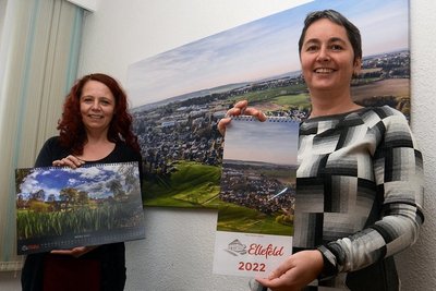 Heike Strauch-Laschewski (links) und Kathrin Kerber mit der ersten Ausgabe von Bildkalender und Küchenkalender. Hinter ihnen die Ortsansicht, fotografiert von Mathias Seidel, die die Titelseite ziert.