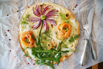 Kreativer Pizza-Belag: Mit roten Zwiebelstreifen, Rucola und Dill sowie  Lachs- und Zucchini-Röschen entsteht im Handumdrehen eine Blumenwiese zum Essen.