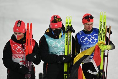 Manuel Faisst (l-r), Julian Schmid und Vinzenz Geiger aus Deutschland halten eine deutsche Flagge in den Händen. Teamkollege Eric Frenzel kann bei der Siegerehrung nicht dabei sein, da er medizinische behandelt werden muss.