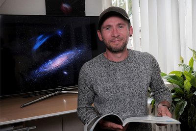 Hat gut lachen: Amateurastronom Marcel Drechsler aus Bärenstein gehört zu den Astrofotografen des Jahres. Im Hintergrund das Siegerbild in der Kategorie Galaxien: der Plasmabogen bei der Andromeda-Galaxie. Damit hat der Erzgebirger mit seinem Team zuletzt die Fachwelt überrascht.