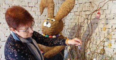 Annie Porstmann schmückt einen Strauß neben dem großen Osterhasen aus Stroh mit Ostereiern, die teils mit christlichen Motiven verziert worden sind. 