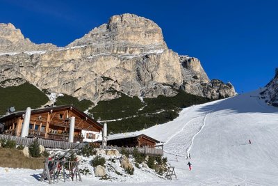 Neben der Edelweißhütte in Alta Badia führt eine schwarze Piste herunter. Dahinter die typischen Felsen der Dolomiten, die sich in den Abendstunden rötlich färben.
