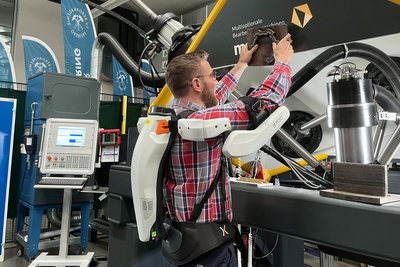 Sebastian Bieber demonstriert, wie das Exoskelett den Körper beim Heben und Anbringen schwerer Gegenstände unterstützt.