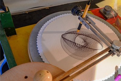 Unter dem automatisch kreisenden Stift der Kritzelmaschine entstehen fantastische Schlaufenmuster, die wie gedruckt wirken.