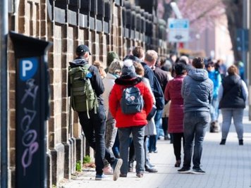 Menschen stehen außerhalb der Uniklinik in einer Warteschlange zum Eingang der Corona-Ambulanz. 