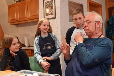 Stefan Gräßler zeigt Josefine, Jule und Jamie, wie ein Gesicht bemalt wird. Dazu schneidet er zur Verdeutlichung auch Grimassen.