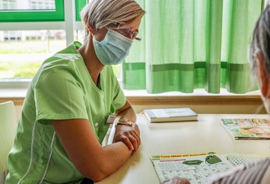Stefanie Jahr lässt sich im Krankenzimmer von Patientin Renate Baum ein Rätselheft erklären. 