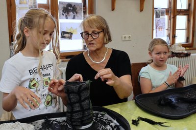 Hanna (l.) stülpt zusammen mit Sabine Brockhage ihren noch nassen Schlossturm über einen Becher, wo die Wolle dann trocknen muss. Elise (r.) formt bereits die langen Spinnenbeine.