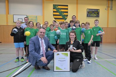 Landrat Rico Anton (vorn l.) hat das „Ehrenamt des Monats“ an Lena Neumeier (vorn r.) verliehen, die sich für den Handball-Nachwuchs stark macht.