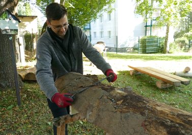 Marcus Gillner entrindet eine Baumstammhälfte. Daraus fertigen AGH-Teilnehmer Bänke, die an Wanderwegen um Zschopau aufgestellt werden. 