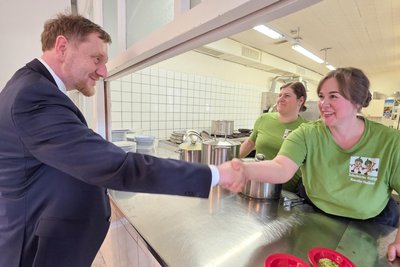 Sachsens Ministerpräsident Michael Kretschmer wird von Schulküchen-Betreiberin Karolin Meßner begrüßt.