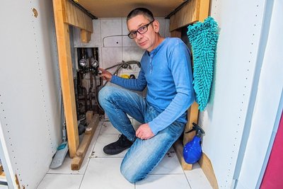 Vater Daniel Kunel zeigt das Problem: Hinter den Fliesen sind die alten, störanfälligen Rohre aus den 1950-er Jahren. Wasser gibt es aber zumindest, weil notdürftig repariert. 