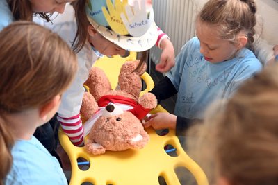 Der Teddy muss auf einer Trage durch einen Parcours getragen werden, dafür wird er mit Binde festgebunden.