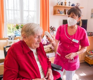 Routine für Pflegefachkraft Cornelia Schneider: Sie kontrolliert die Körpertemperatur bei den Bewohnern - wie hier bei Hilde Schreiter. Die 89-Jährige wünscht sich, dass endlich die Bereichstrennung wieder aufgehoben wird, um ihre Freundin im Erdgeschoss treffen zu können.