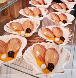 Macadamia-Madeleines in Safran-Schokocremé mit Schoko-Spritzmuschel und einer Fondantperle.