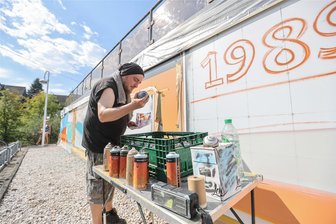 100 Jahre Sommerbad Garnsdorf: Zeitreise in elf Bildern mit 60 Farben - Graffitikünstler Markus Esche hat sein Hobby zum Beruf gemacht und arbeitet bei der Firma Rebel Art, die Fassaden gestaltet. An der Kegelbahn des Sommerbades Garnsdorf sprüht er mit weiteren Kollegen die 100-jährige Geschichte der Freizeitstätte auf. Hier beleuchtet er die Epoche 1993/94, als das Bad umfassend saniert wurde.