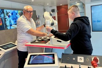 1000 Euro Willkommensprämie: Wie ein Unternehmen aus dem Erzgebirge um Azubis wirbt - Einen Cobot (Industrieroboter) testet der Achtklässler Yannik Dürr gemeinsam mit dem Berater Andreas Ottenberg im Inneren des Informationstrucks.