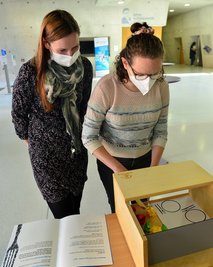 Reporterin Lea Becker (r.) versucht sich am Mittagessen, Studentin Bianka Hammer erklärt, was zu tun ist. Die Holzkiste samt Spiegel sorgt für erschwerte Bedingungen. 