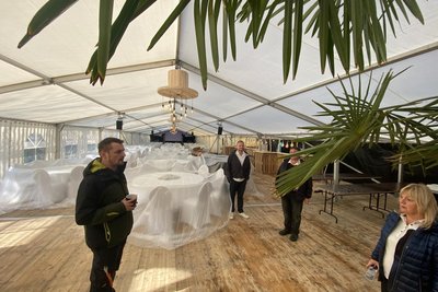 Blick ins riesige Festzelt. Ganz hinten die Bühne für die Livemusik, rechts mehrere, aus Holz rustikal zusammengezimmerte Bars und vorn Platz für spielende Kinder. Abgerundet wird das Ganze von chilligen Sitzecken – unterm Palmenwedel zum Beispiel.