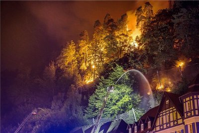 Flammen lodern direkt hinter Häusern im böhmischen Hrensko, während ein Feuerwehrmann zu löschen versucht. 