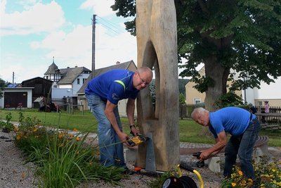 Die Holzplastik "Dreieinigkeit" - Frank Seidel (links) und Georg Gräßler bei der Montage auf dem Dorfplatz am Feuerwehrdepot - markiert Start und Ziel des Rundwanderweges, den der Traditionsverein Feuerwehr in Schreiersgrün anlegt. Bis zur Einweihung des Weges zur Kirmes im Oktober sind auch neun Stationen der Tour fertig. 