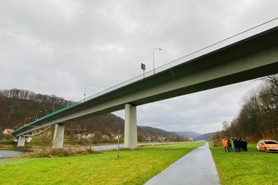 Brücke vor Flusslandschaft, im Hintergrund das Unterspannband in der Mitte der Brücke, das an eine Wippe erinnert.