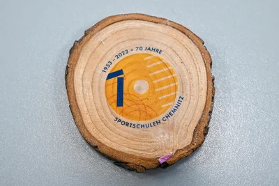 Das Logo "70 Jahre Sportschulen" auf einer Holzscheibe.