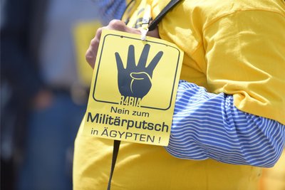 Ein Gegner des Besuchs des ägyptischen Präsidenten in Berlin demonstriert im Juni 2015 vor dem Paul-Löbe-Haus. An seinem T-Shirt trägt er ein Schild mit der Aufschrift „Nein zum Militärputsch in Ägypten“ mit dem R4bia-Emblem.