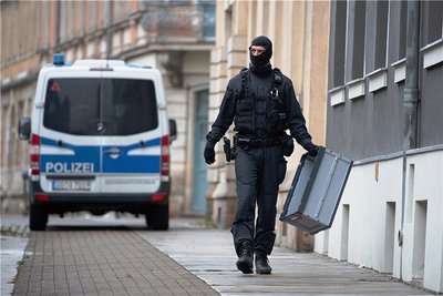 Ein Polizist geht mit einer Transportbox vor einer Häuserzeile im Stadtteil Pieschen entlang. 