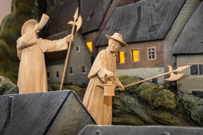 Alle Figuren, wie hier die Nachtwächter, sind aus unbehandelter Linde gearbeitet und nicht bemalt. Anders als die Häuser und Bäume, die als Silhouetten farbig dargestellt sind - nachempfunden den alten geprägten Papierkrippen.