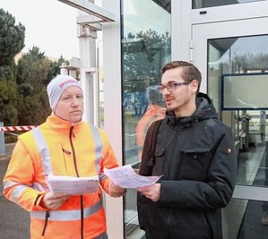 Ein Betriebsratsmitglied (l.) verteilt vor dem Betriebstor einen Flyer an Mitarbeiter Robin Rolf.