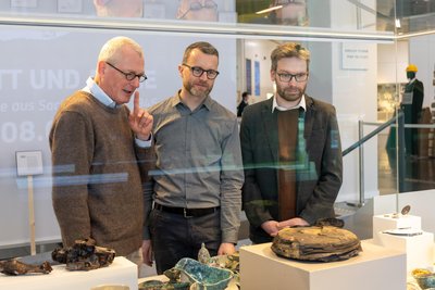 Dr. Michael Strobel, Marcus Sonntag und Dr. Alexander Walther stehen an einer Vitrine mit Fundstücken aus Chemnitz und Dresden.