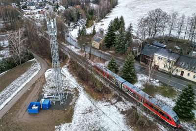 Ein Zug der Erzgebirgsbahn fährt auf der Forschungs- und Erprobungsstrecke durchs Erzgebirge an einem neu errichteten Mobilfunkmast vorbei.