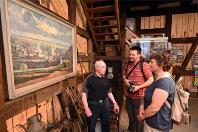 Gottfried „Bub“ Porstmann, ältester Bergmann mit 95 Jahren, berichtet Iris und Frank Manthey von seinem Berufsleben im Bergbau. Die Gäste stehen vor einem Ölgemälde, das Halsbrücke mit Hoher Esse um 1900 zeigt.