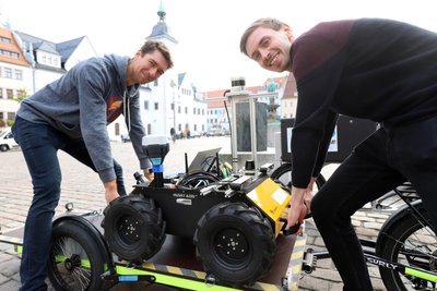 Die wissenschaftlichen Mitarbeiter an der TU Bergakademie Freiberg, Norman Seyffer (l.) und Lorenzo Neumann, heben den Testroboter auf den Obermarkt.