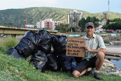 Sebastian Engel mit einem Pappschild, das auf die Müllproblematik im argentinischen Villa Carlos Paz aufmerksam machen soll. Der Text: "Der Müll, den Sie wegwerfen, spricht nicht, aber er sagt viel über Sie aus." 