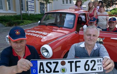 Ein besonderes Kennzeichen für ein besonderes Auto: Gerd Winterstein (rechts) von der Zulassungsstelle in Aue überreicht Horst Löscher von der Trabantfeuerwehr Grüna das letzte ASZ-Nummernschild. 