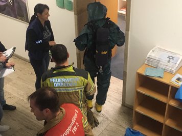 Ein Feuerwehrmann mit Schutzanzug geht in das Zimmer des Sicherheitsbeauftragten vom Landtag, in dem Schreiben bis zum Eintreffen von Polizei und Feuerwehr sichergestellt wurde.