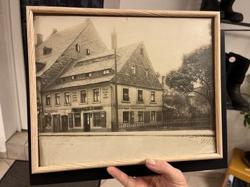 Eine schwarz-weiß Fotografie des Gebäudes zeigt, wie klein der ehemalige Verkaufsraum war. Das, was heute Ladenfläche ist, war früher zweigeteilt. Rechts "Schuh-Wagner", links ein Friseur.