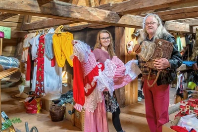 Gunnar Rug und Juliane Röber inmitten der Requisiten und Kostüme. Er zeigt einen Drachenkopf aus Körben, sie ein Kleid. 