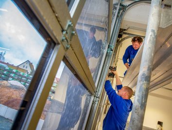 Im Inneren des zukünftigen Feuerwehrdepots sind Elektrotechniker der Frankenberger Beyer & Lohs GmbH dabei, die Installation der Torantriebe der Fahrzeughalle zu montieren.