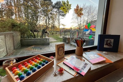 Blick durch ein Fenster in den Garten. Rechts außen: ein Bildnis von Friedrich Fröbel.